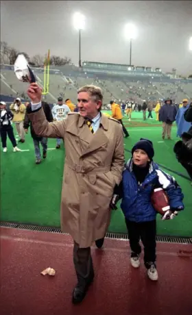  ?? John Beale/Post-Gazette ?? Pitt football coach Johnny Majors tips his cap to cheering fans as he leaves Pitt Stadium after a victory over Rutgers in November 1996. Carrying the game ball for Mr. Majors is his grandson, Brandon. It was Mr. Majors’ last game as coach at the university.