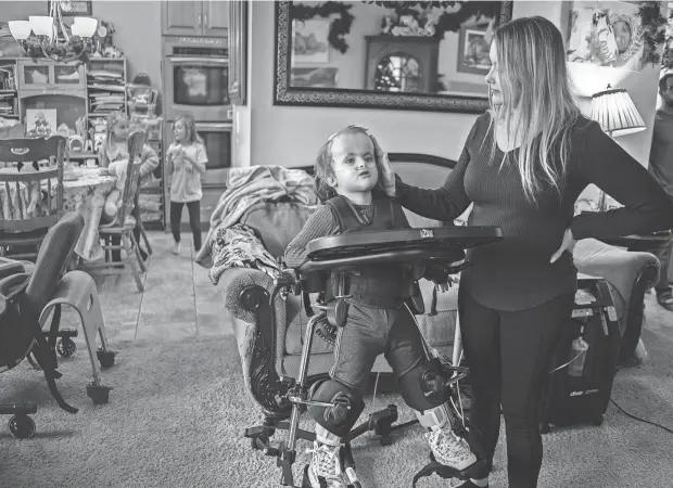  ?? PHOTOS BY RYAN GARZA/DETROIT FREE PRESS ?? Jewel Calleja, of Livonia, stands with her daughter, CC Calleja, 4, as she is secured in a stander to help with her leg strength, circulatio­n and digestion in the living room of their home on Friday as they watch the television. CC was born with Trisomy 18 and despite intense pressure to terminate the pregnancy, the Callejas decided against it. While many physicians advise families that children born with Trisomy 18 won’t make it out of the hospital, CC is growing up at home and her family is finding ways to meet her medical needs.