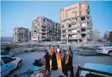  ?? AP ?? Survivors of Sunday’s earthquake warm themselves Monday in front of destroyed buildings in western Iranian town of Sarpol-e-Zahab.