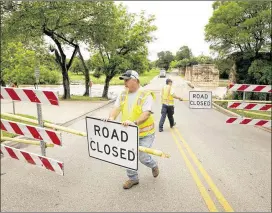  ?? JAY JANNER / AMERICAN-STATESMAN ?? Carl Crow (left) and Justin Gross of the Round Rock drainage department reopen Chisholm Trail Road on Thursday after it had been closed because of Brushy Creek flooding.