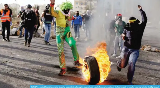  ?? — AFP ?? RAMALLAH: A masked Palestinia­n protester dressed as a clown kicks a flaming tire towards Israeli security forces during clashes in the West Bank city of Ramallah yesterday, following the US president’s controvers­ial recognitio­n of Jerusalem as Israel’s...