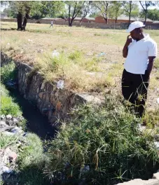  ??  ?? A man looks at a heavily polluted stream that flows past Lotshe Primary School in Bulawayo. The stream is fast filling up with grass and litter (Picture by Dennis Mudzamiri)