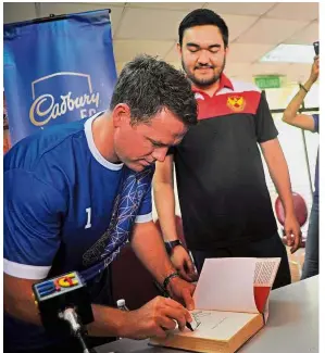  ?? — AFIQUE YUSOFF/The Star. ?? Inked: Michael Owen signing a book as a memento of his visit at a Selangor Under-19 football clinic yesterday. Looking on is the Tengku Mahkota of Selangor Tengku Amir Shah ibni Sultan Sharafuddi­n Idris Shah.