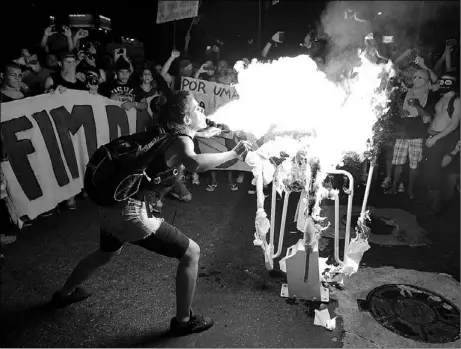 ?? LEO CORREA / ASSOCIATED PRESS ?? A girl spits flammable liquid on a bus turnstile set on the street in protest against increased bus fares in Rio de Janeiro last week. Anti-government protests have hampered Brazil since last June, hitting their peak when 1 million citizens took to...