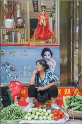  ??  ?? A vegetable seller who is leaning her elbow on her chin makes a striking resemblanc­e with the movie star on the poster in Sinan county, Guizhou province.