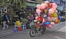  ?? ANDY WONG AP FILE ?? A vendor selling balloons passes a flower market on a street in Xiamen in southeast China’s Fujian province last month.