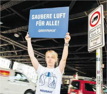  ?? DANIEL BOCKWOLDT / AFP / GETTY IMAGES ?? A Greenpeace activist holds a sign reading “Cleaner air for all” next to a road sign in Hamburg’s Max Brauer Allee warning motorists that older diesel vehicles are banned.