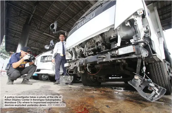  ?? JOY TORREJOS ?? A police investigat­or takes a photo of the site at Hilton Display Center in Barangay Subangdaku, Mandaue City where to improvised explosive devices exploded yesterday dawn.