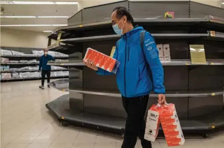  ?? GETTY IMAGES ?? SCARCE SELECTION: A man wearing face mask carries tissue paper in front of empty shelves inside a grocery store on Feb. 9 in Hong Kong, China. Experts say people in the U.S. should stock up on needed supplies now rather than get stuck if there’s a run on items later on.