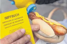  ?? FOTO: HENDRIK SCHMIDT/DPA ?? Ein Mann hält am mobilen Impfzentru­m im sächsische­n Aue seinen Impfpass und eine Bratwurst im Brötchen, die es als Impfanreiz gab.