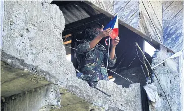  ?? AFP ?? A Philippine soldier holding a miniature national flag inside a bullet riddled house in Butig town, Lanao del Sur province, in the southern island of Mindanao, one week after gunmen waved black flags of the Islamic State group and attacked a military...