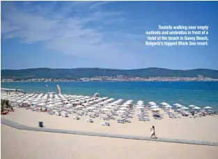  ??  ?? Tourists walking near empty sunbeds and umbrellas in front of a hotel at the beach in Sunny Beach, Bulgaria’s biggest Black Sea resort.