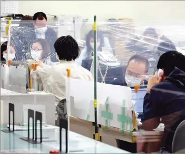  ?? AFP ?? Staff members work behind transparen­t sheets as a preventive measure to stop the spread of Covid-19 at a city hall in Fukaya, Saitama prefecture. In Japan, as many as 2,060 people applied for workers’ compensati­on for mental illnesses caused mainly by job stress in fiscal 2019.