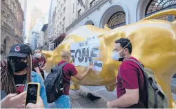  ?? ANDRE PENNER/AP ?? Activists paste the Portuguese word “hungry” on the Golden Bull on Nov. 17 outside the Brazilian B3 Stock Exchange in Sao Paulo, Brazil.