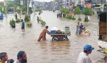  ?? AFP ?? Commuters cross a flooded street after heavy rains in Lahore yesterday.