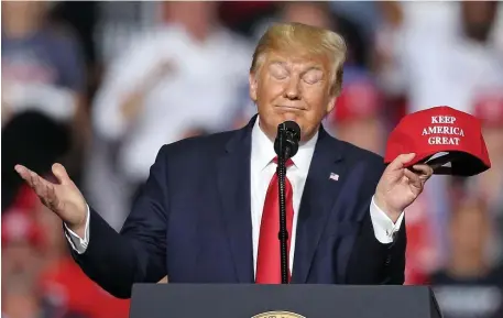  ?? Matt stone / Herald staff file ?? ‘A BIG EFFORT’: President Trump holds a hat with his new slogan ‘Keep America Great,’ during a rally at SNHU Arena on Aug. 15, 2019, in Manchester, N.H. In his visit to the Granite State this weekend, attendees will be encouraged to wear a provided mask, which wasn’t an issue at his August visit, below.