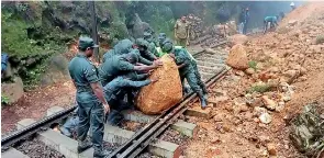  ?? ?? Army personnel clear a rock boulder after a mound of earth fell on tracks near the Diyathalaw­a Railway Station. Pic by Nayananand­a Buwaneka