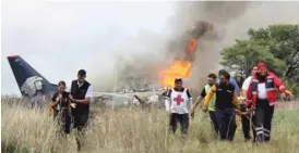  ?? RED CROSS DURANGO VIA AP ?? Rescuers carry a person on a stretcher as airline workers (left) walk away from the site of Tuesday’s Aeromexico airliner crash near Durango, Mexico.