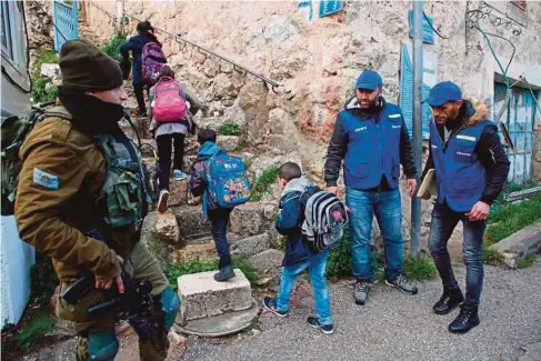  ??  ?? TENTERA Israel yang berkawal di Tebing Barat memerhati anggota sukarela Palestin mengiringi murid pulang dari sekolah di Hebron, kelmarin. - AFP