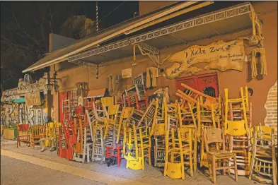  ??  ?? A cat stands near colored chairs and tables stored outside a closed traditiona­l restaurant in Monastirak­i, a district of Athens.