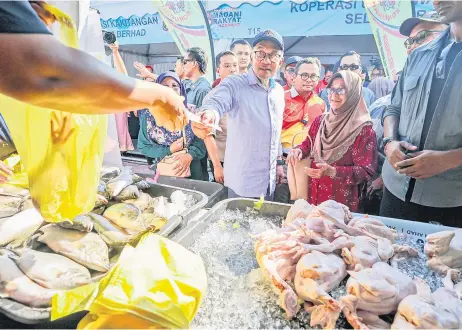  ?? — Bernama photo ?? Anwar helps a visitor pay for her purchase at a stall during a tour of the Central Zone Madani Rakyat Programme grounds.