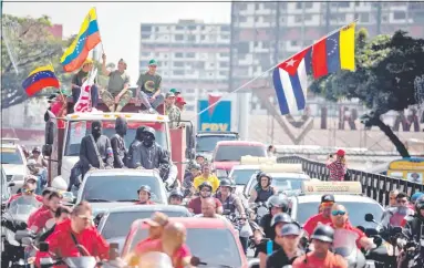  ??  ?? Encapuchad­os y armados, líderes paramilita­res chavistas lideran una marcha de grupos de choque, a la sombra de la bandera de la dictadura cubana, que ha montado el aparato represivo en Venezuela.