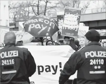  ?? Maurizio Gambarini AFP/Getty Images ?? GERMAN POLICE OFFICERS stand guard in front of protesters with placards and banners Friday in Berlin during a demonstrat­ion calling for online retail giant Amazon to pay its employees fair wages.