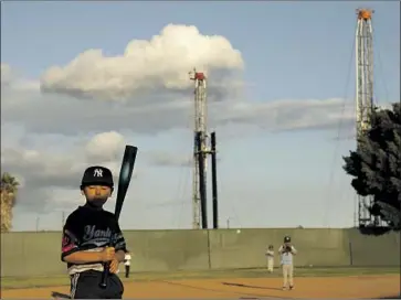  ?? Photograph­s by Genaro Molina Los Angeles Times ?? BENNY ESCOBAR, 7, and others play at John Mendez Baseball Park in Wilmington amid towering oil rigs.