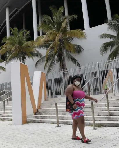  ?? AP ?? OUTBREAK: A woman wearing a protective face covering walks past Marlins Park on Monday. Upwards of 13 Marlins players tested positive for the coronaviru­s on Monday, forcing teams to postpone games.