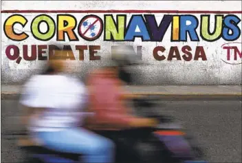  ?? REBECCA BLACKWELL AP ?? A couple rides a motorcycle past a painted sign reading in Spanish “Coronaviru­s. Stay Home,” in Iztapalapa, Mexico City. The number of cases in Mexico has been growing.