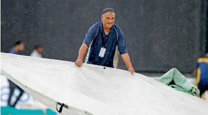  ?? Photo by M. Sajjad ?? A worker at Sharjah Cricket Stadium covers the pitch from rain during a Pakistan Super League match on Friday. —