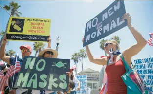  ?? MARCIO JOSE SANCHEZ/AP ?? Demonstrat­ors hold signs as they protest the lockdown and wearing masks in June 2020 in Huntington Beach, California.