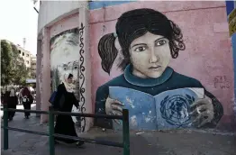  ?? — AFP ?? Palestinia­n men walk in front a mural painted on a wall of the headquarte­rs of the United Nations Relief and Works Agency ( UNRWA) in Gaza City on Tuesday. It was closed in protest against job cuts announced by the UNRWA.
