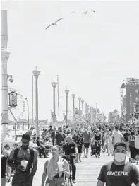  ?? ALEX EDELMAN/GETTY-AFP ?? Dozens of people, some with masks, some without, stroll along the boardwalk Saturday in Ocean City.