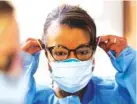  ?? AP FILE PHOTO/ELAINE THOMPSON ?? A respirator­y therapist pulls on a second mask over her N95 mask as she gets ready to go into a patient’s room in the COVID-19 Intensive Care Unit at a hospital in Seattle.