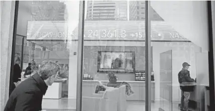  ?? Stephan Savoia, The Associated Press ?? A passer-by peers in the window while investors congregate inside the Fidelity Investment­s office on Congress Street in Boston on Tuesday as the ticker displays stock market numbers.