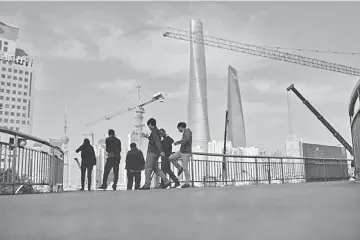  ??  ?? People walk on a bridge near the financial district of Pudong in Shanghai. Local officials in China are dithering over project approvals and business deals, some to avoid the spotlight of an anti-corruption campaign, impeding Beijing’s plans to use...