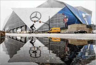  ?? JOHN SPINK/JSPINK@AJC.COM ?? Work continued to place Super Bowl branding on Mercedes-Benz Stadium as the facade reflected in puddled water along Martin Luther King Jr. Drive in downtown Atlanta on Friday.