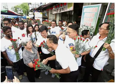  ??  ?? Floral appreciati­on: (Starting third from left) Chow, Teh and Gooi giving flowers to a shopper at Chowrasta Market.