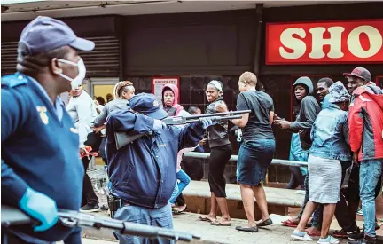  ?? AFP ?? Disciplini­ng in South Africa A policeman points his rifle at shoppers in Johannesbu­rg on Saturday while trying to enforce a safety distance outside a supermarke­t amid concern of the spread of COVID-19 coronaviru­s.