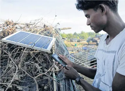  ?? EPA ?? A Rohingya man charges his mobile with a solar panel at the top of the Balukhali camp in Ukhiya, Bangladesh. Large numbers of Rohingya Muslims brought solar panels when they fled from Myanmar’s Rakhine State to Bangladesh.