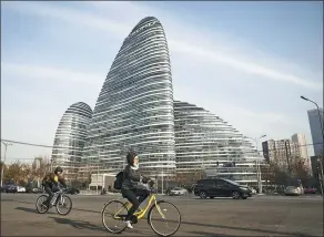  ?? IMAGES QILAI SHEN / BLOOMBERG VIA GETTY ?? Cyclists ride past commercial buildings of a SOHO project in Beijing.