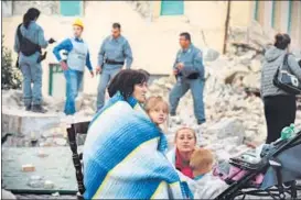  ??  ?? Victims sit among the rubble of a house in central Italy.