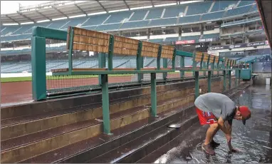  ?? AP PHOTO BY JAE C. HONG ?? Heavy rain falls as a grounds crew member works on a clogged drain in the flooded dugout before a baseball game between the Los Angeles Angels and the Philadelph­ia Phillies, Tuesday, in Anaheim.