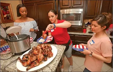  ?? NWA Democrat-Gazette/ANDY SHUPE ?? Sarah Mohammad (center) of Iraq picks out a piece of barbecued chicken Wednesday alongside Elizabeth Kamarade (left) of Rwanda and Sima Niro of Afghanista­n. The three University of Arkansas students were at an Independen­ce Day party hosted by Jhonnie and Bob Taylor at their Fayettevil­le home. The Spring Internatio­nal Language Center paired Fulbright scholars and Mexican teachers with Northwest Arkansas residents to celebrate the holiday.