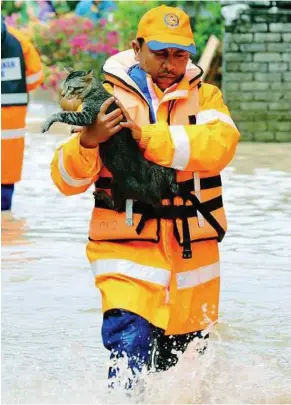  ??  ?? Pity on the kitty: A Civil Defence Department member rescuing a cat from the floods in Kampung Gugusan Manjoi. The cat was stranded at its owner’s inundated home.