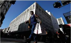  ?? Associated Press ?? Q A man carries shopping bags across the street from a Macy's store Friday in San Francisco. Black Friday once again kicked off the start of the holiday shopping season.