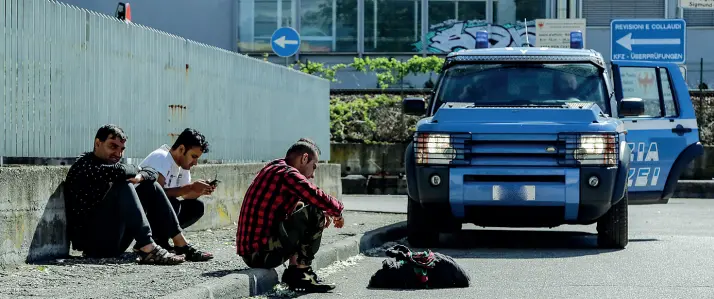  ?? (Foto Klotz/Rensi) ?? Controllo Alcuni richiedent­i asilo all’esterno dell’ex Alimarket, guardati a vista da un mezzo della polizia