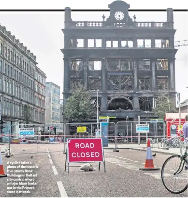  ??  ?? A cyclist takes a photo of the historic five-storey Bank Buildings in Belfast city centre, where a major blaze broke out in the Primark store last week