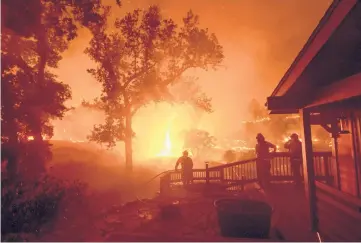  ??  ?? In a year marked by climate-related disasters worldwide, five of the six largest wildfires in California’s history happened in 2020. Above, people watch as flames approach a home Aug. 21 in incorporat­ed Napa County.